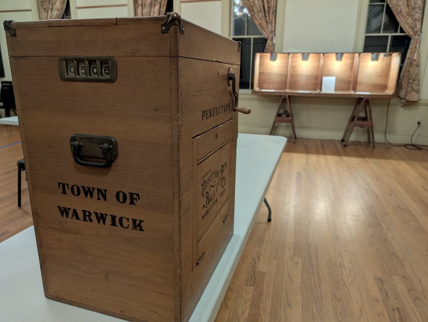 The Warwick ballot box with voter count 506 showing, with the lit voting booths in the background.